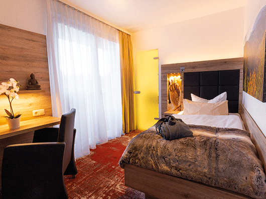 Hotelzimmer mit einem Bett, zusammengefaltetem Bademantel, links Tisch mit Orchidee und einem Sessel